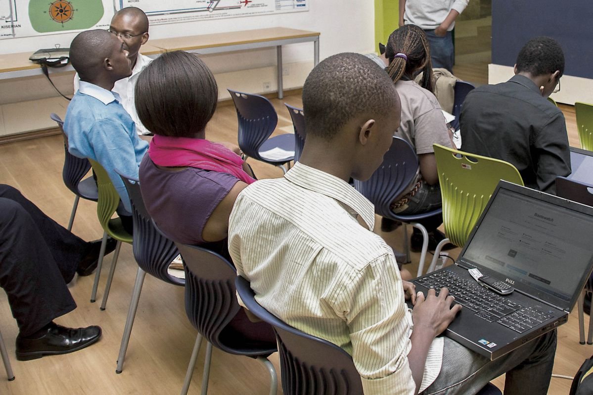 Young people seated in a training room, one of them typing on a laptop